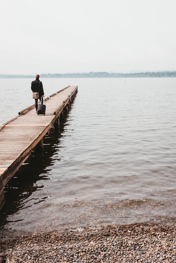 A man walks on a wooden pier by a lake in Seattle, carrying a suitcase.