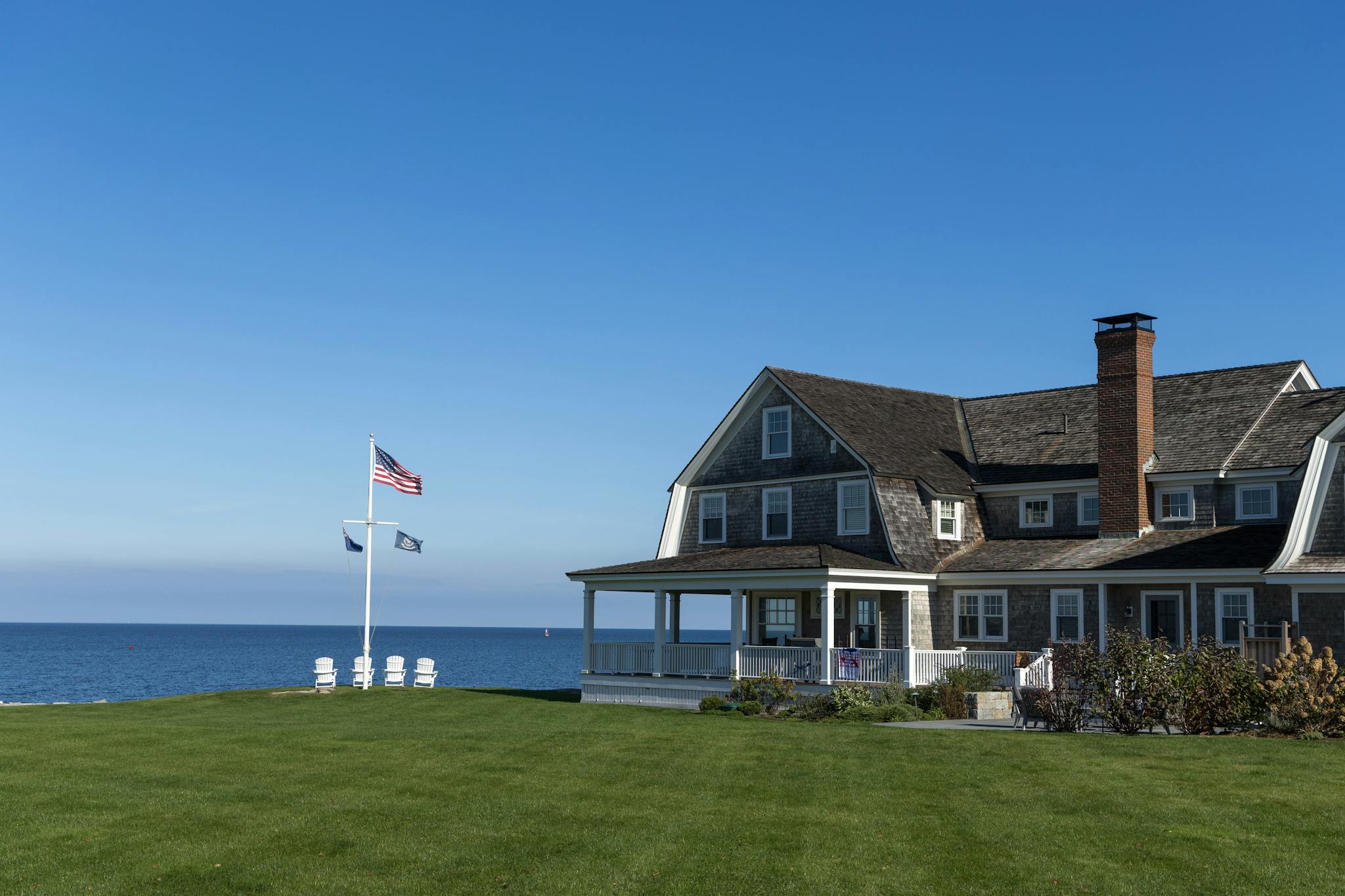 A serene beachfront house with American flag and ocean view under clear blue sky.